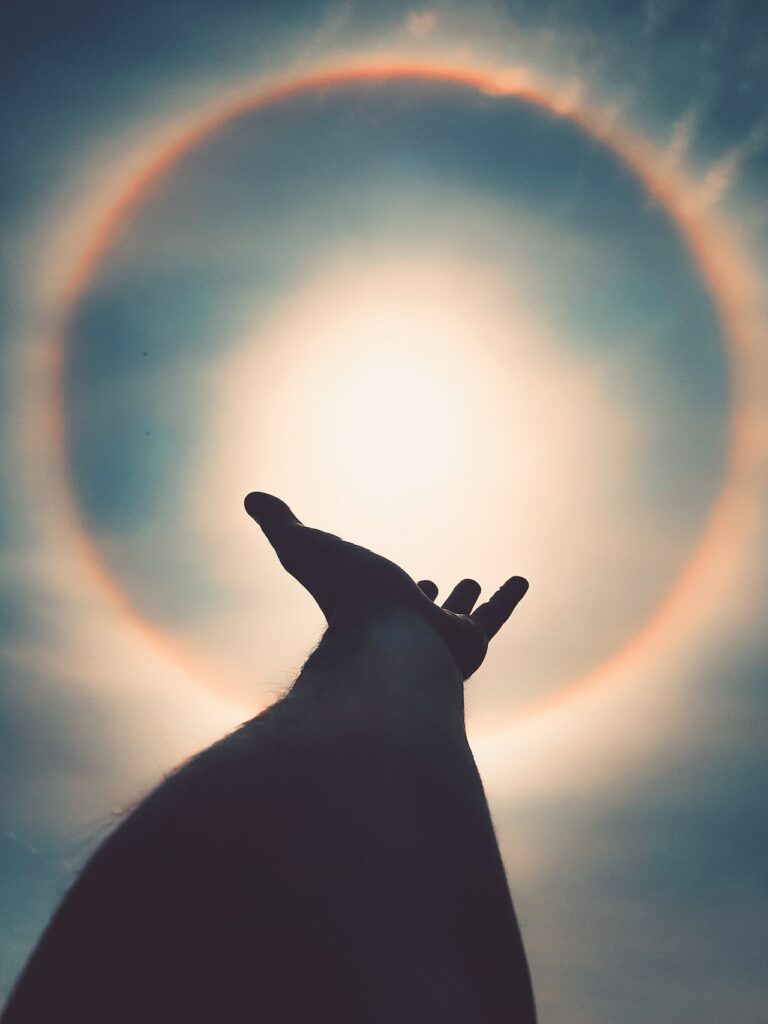 looking up at the silhouette of a hand reaching towards the sun with a hazy halo around it